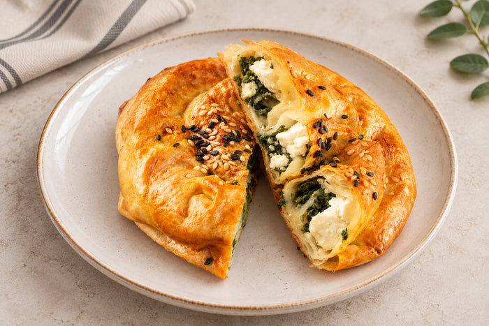 dän spinach & feta burek, golden yufka pastry broken open to show spinach and feta, topped with black and white sesame